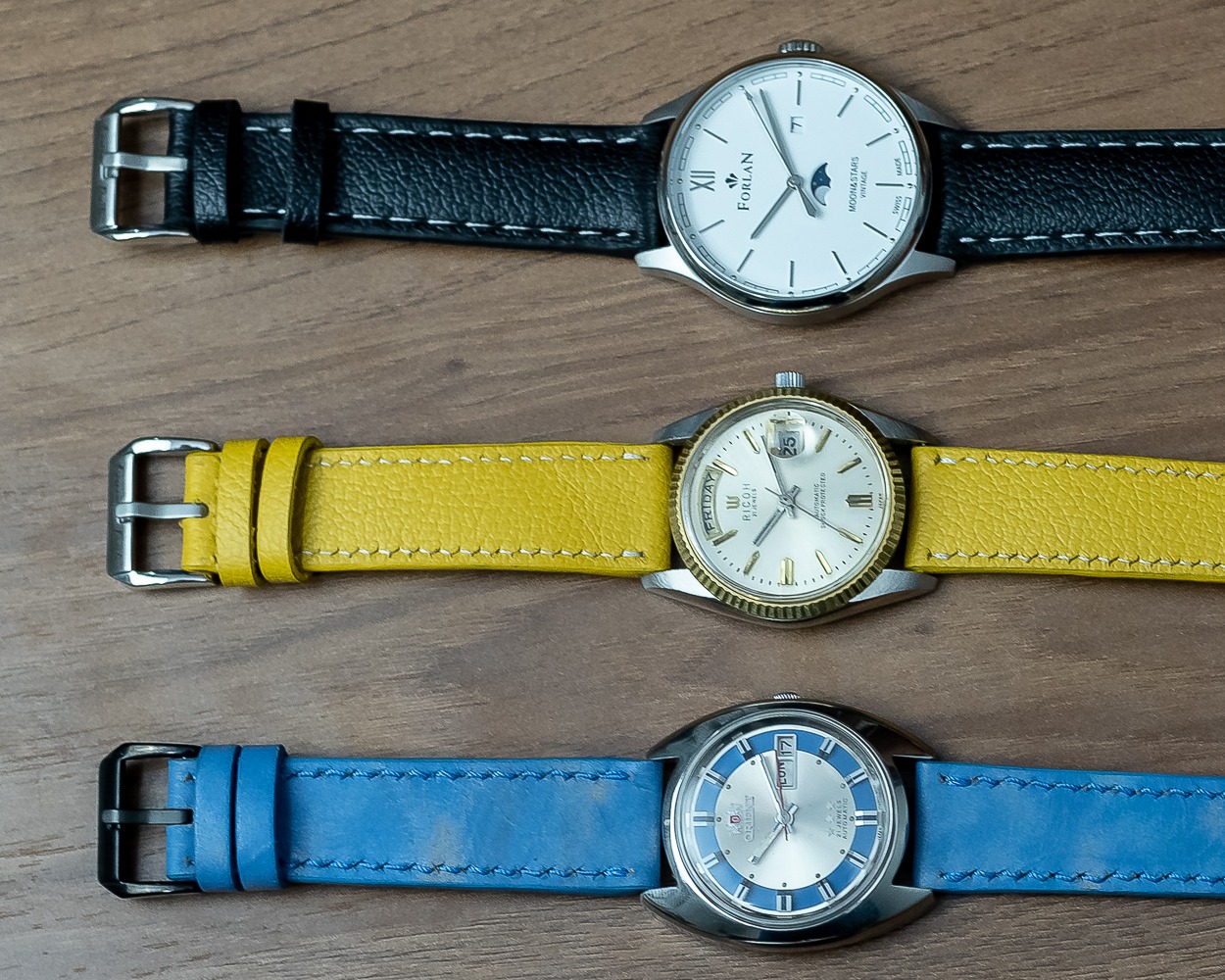 Três relógios com pulseiras de couro preta, amarela e azul feitas à mão
