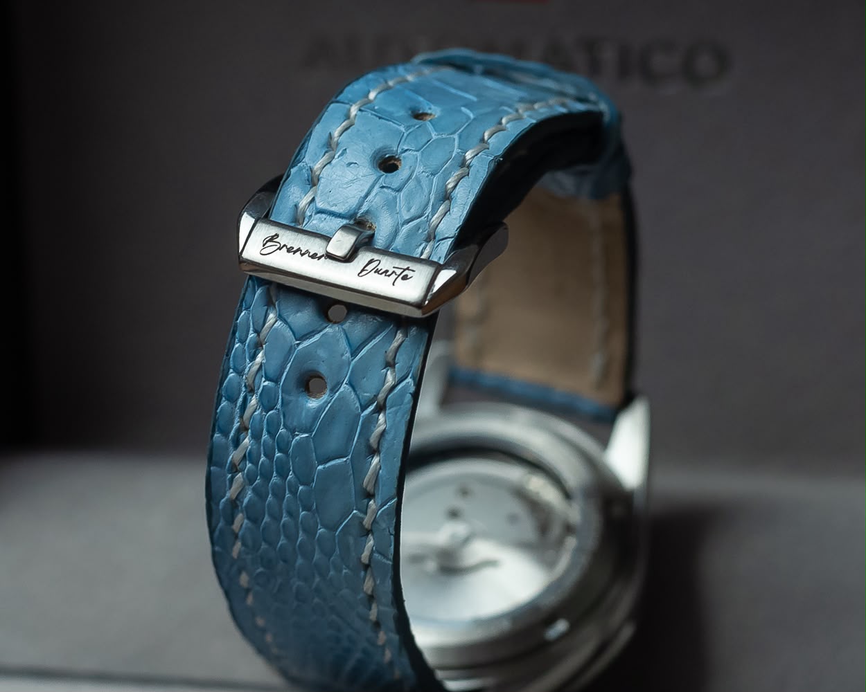Pulseira de couro azul texturizado com fivela gravada Brenner Duarte em relógio automático