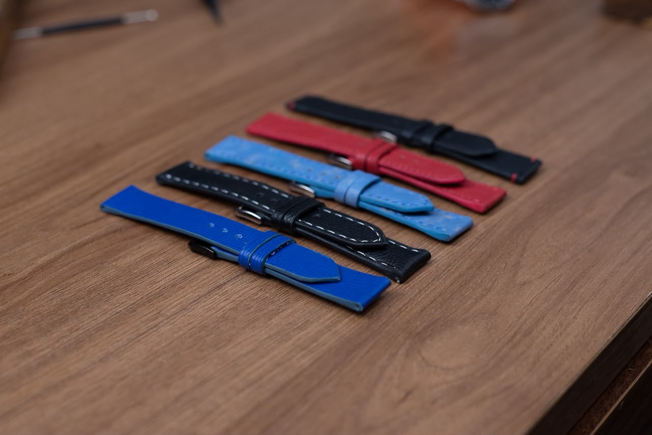 Cinco pulseiras de couro em preto, vermelho, azul-claro e azul royal alinhadas sobre a bancada
